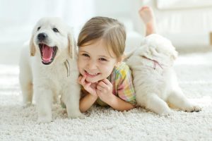 Picture of girl and two puppies laying on the rug