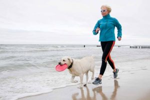 Picture of a woman running on the beach with a dog