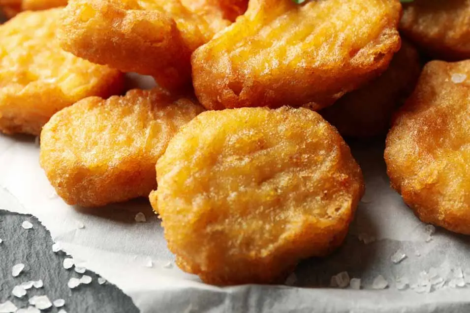 Close-up of crispy golden chicken nuggets with a crunchy coating, sprinkled with coarse salt and served fresh on parchment paper.