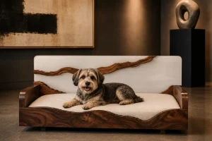 Luxury walnut and white resin dog bed with flowing live-edge details, a plush cream cushion, and a happy mixed-breed dog in a contemporary art gallery.