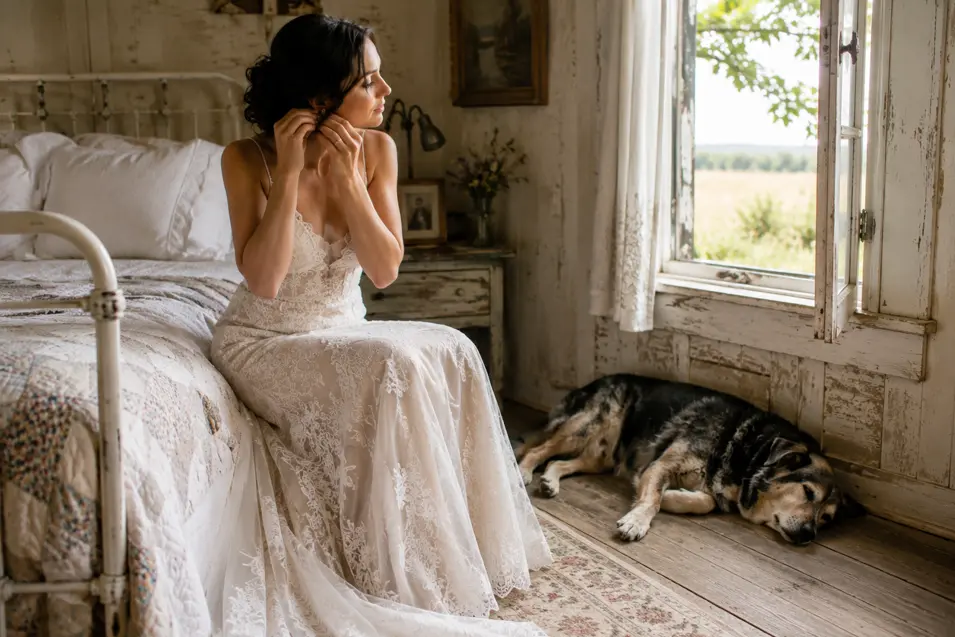 A bride gets ready in a rustic farmhouse bedroom while her dog sleeps peacefully by the open window.