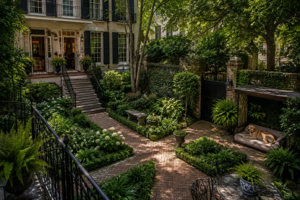 Lush, shaded courtyard garden with brick paths, elegant greenery, wrought iron details, and a dog relaxing on a cozy outdoor bed.